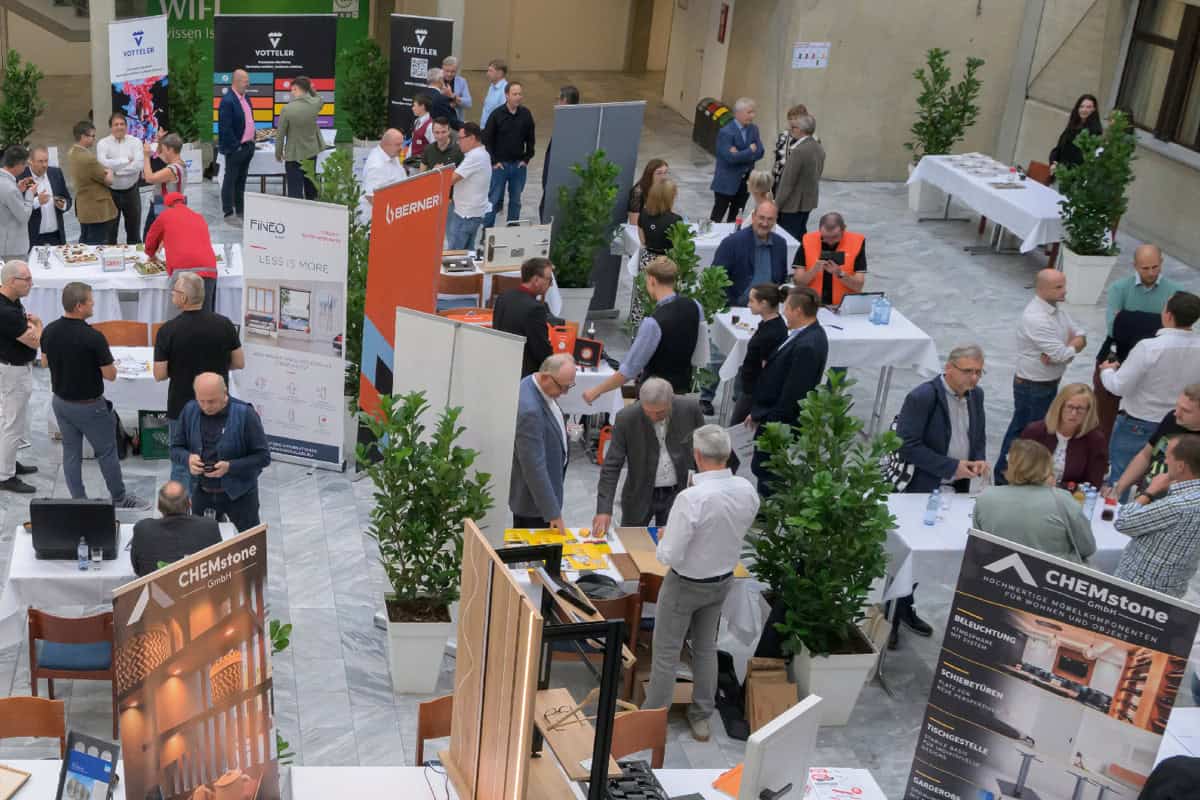 Landesinnungstagung 2026 – „Miteinander“ im Mittelpunkt Blick von oben auf die Fachausstellung im Rahmen der Landesinnungstagung der NÖ Tischler 2026. Zahlreiche Besucherinnen und Besucher tauschen sich an den Messeständen verschiedener Unternehmen über Produkte und Lösungen für das Tischlerhandwerk aus. Zwischen den Ausstellungsflächen stehen Stehtische und grüne Pflanzen.