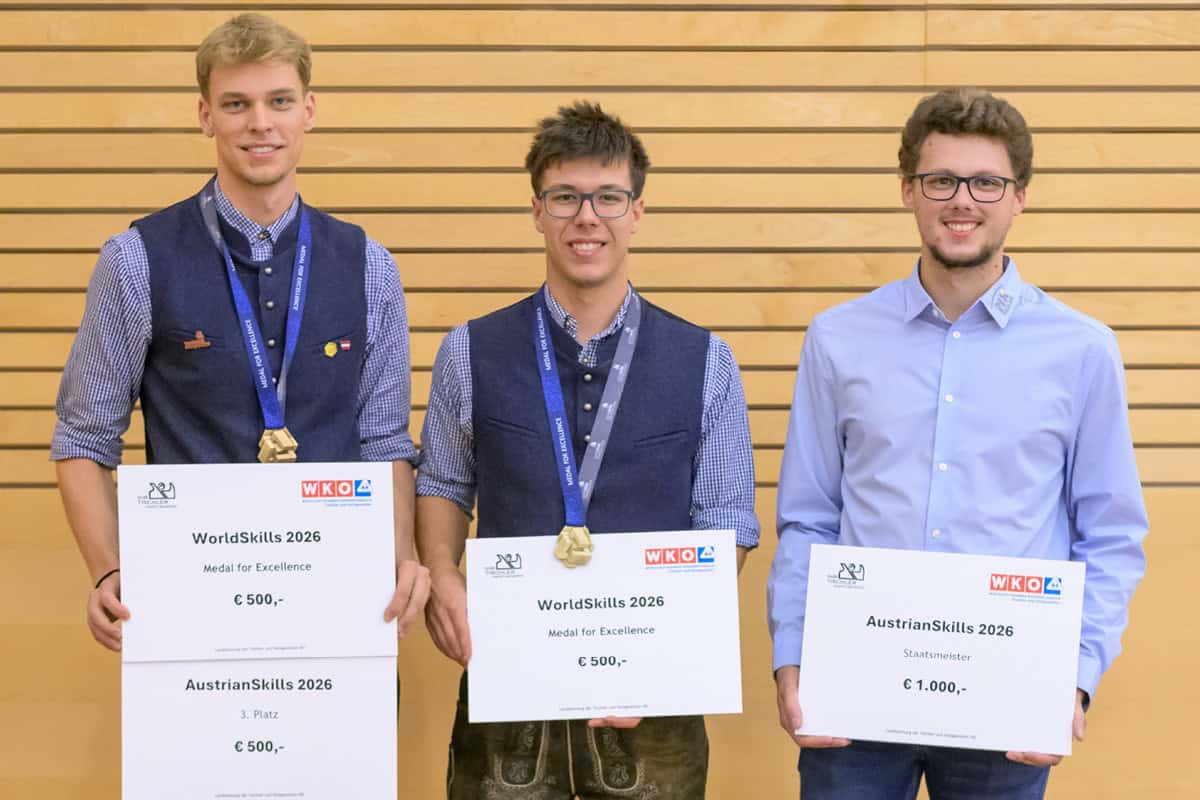 Landesinnungstagung 2026 – „Miteinander“ im Mittelpunkt Drei junge Preisträger der Tischlerbranche stehen mit Urkunden vor einer hellen Holzwand. Zwei von ihnen tragen Medaillen für ihre Leistungen bei den WorldSkills 2026, der dritte wurde bei den AustrianSkills 2026 als Staatsmeister ausgezeichnet.